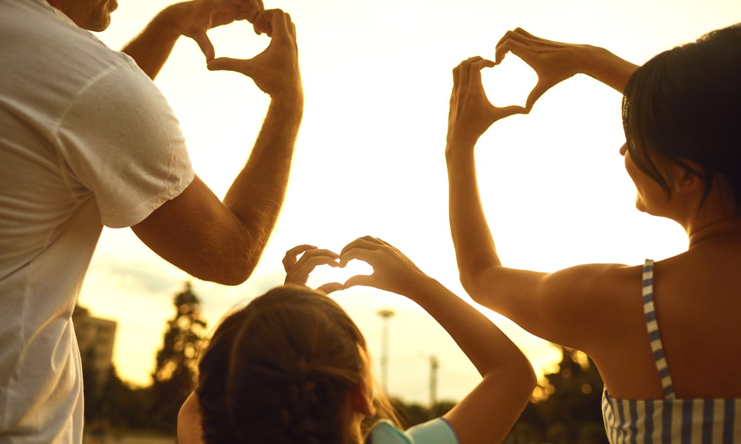 Family support making heart shapes with hands against a sunset background.