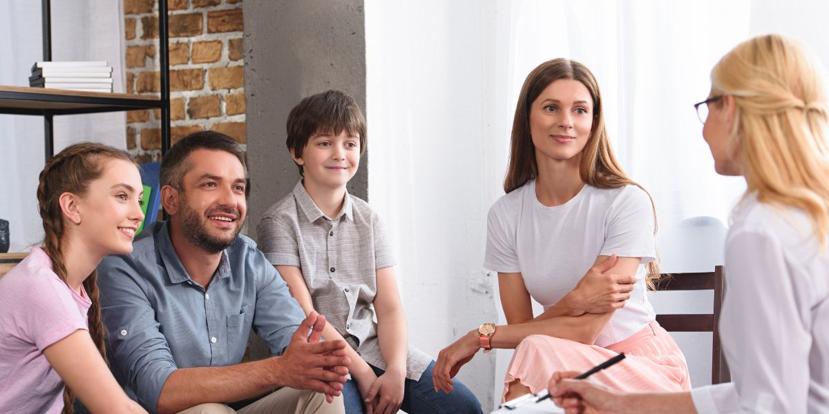 Family of four talking with a therapist in a bright, comfortable room.