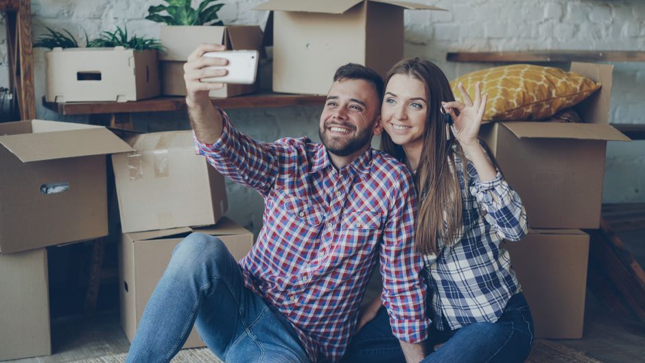 A smiling couple stands proudly in front of their beautiful, modern first home, representing the stability and wealth built through sobriety and smart financial moves.